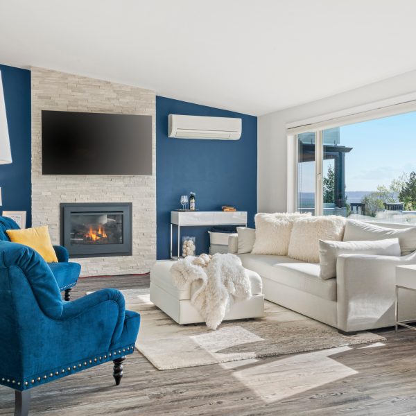 Welcoming living room with a blue accent wall, white faux fur pillows and a modern stacked stone fireplace